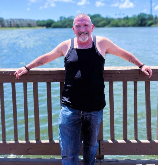 An image of Psychic Ivan leaning against the railing of a fence, a beautiful expanse of blue water stretching beyond him.